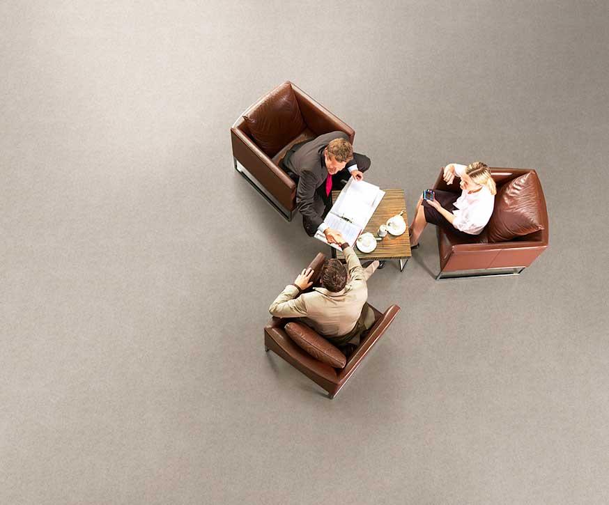 Aerial view of four people having a business meeting, seated in leather chairs around a square table.
