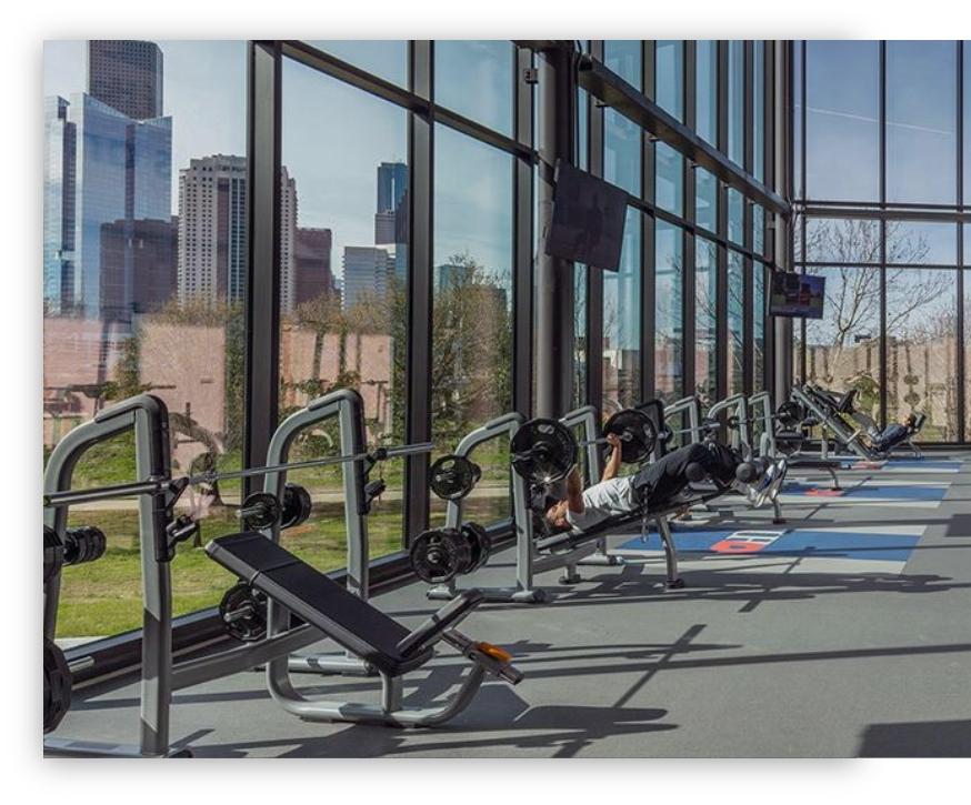 Gym with a line of weight benches in front of floor-to-ceiling windows overlooking the city skyline.