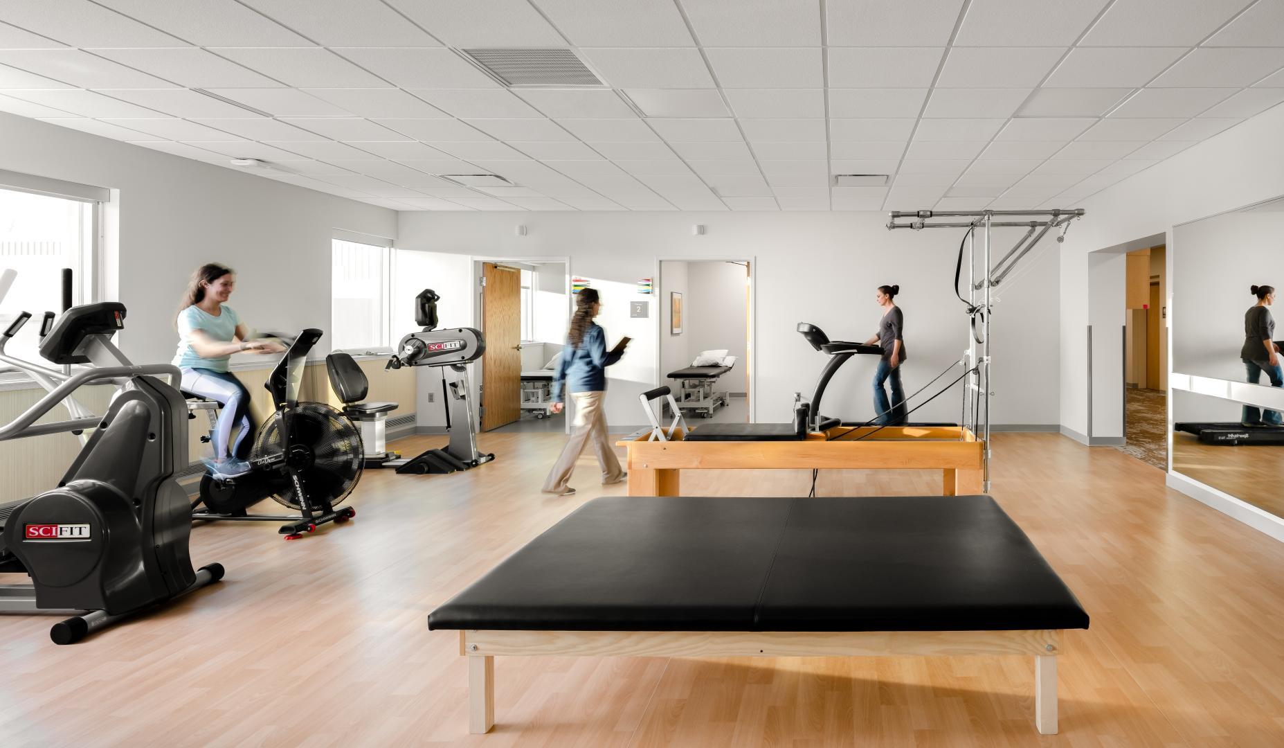 Physical therapy room with multiple exercise machines and patients exercising.