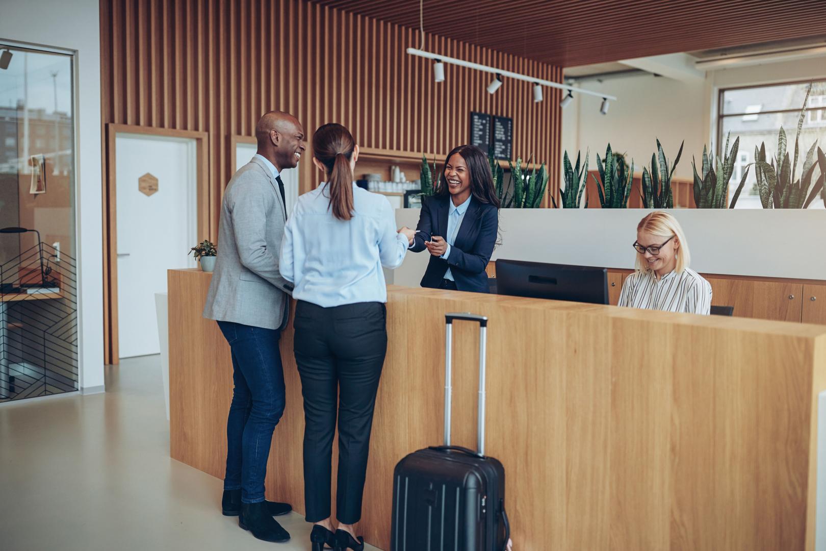 Business colleagues at a modern hotel reception desk, with a receptionist smiling.