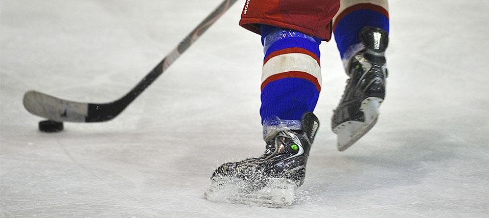 Close-up of a hockey player's skates on ice, controlling a puck with a stick
