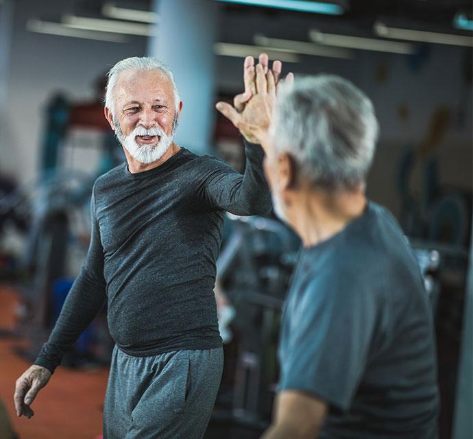 An older man high-fiving another older man as he completes his workout in a fitness studio. 