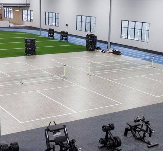 Two indoor badminton courts side by side in an indoor fitness center with exercise equipment and artificial turf nearby. 