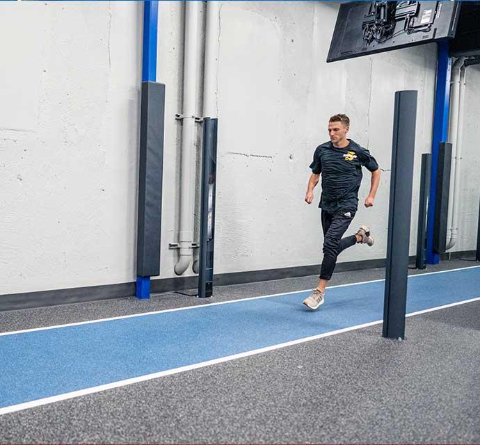 Man sprinting along a blue lane in a modern indoor gym with white walls.