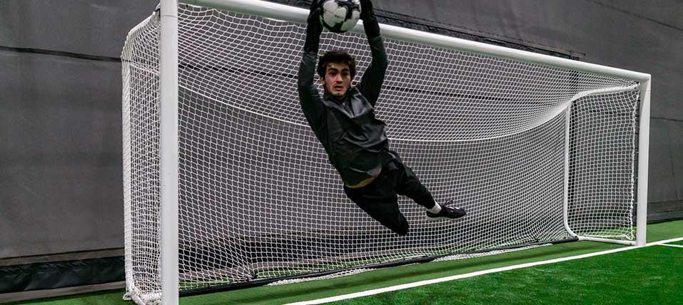Goalie leaping to make a save on an indoor soccer field. 