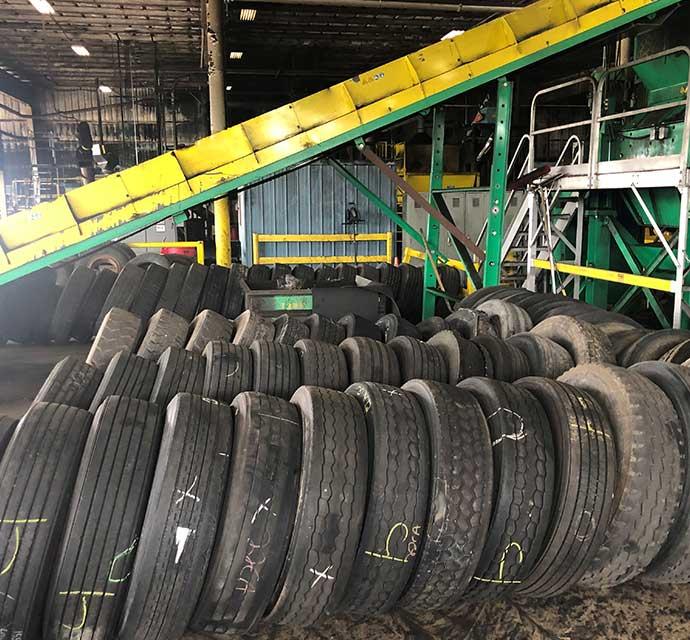 Stack of used tires in a recycling facility with conveyor belts and industrial equipment.