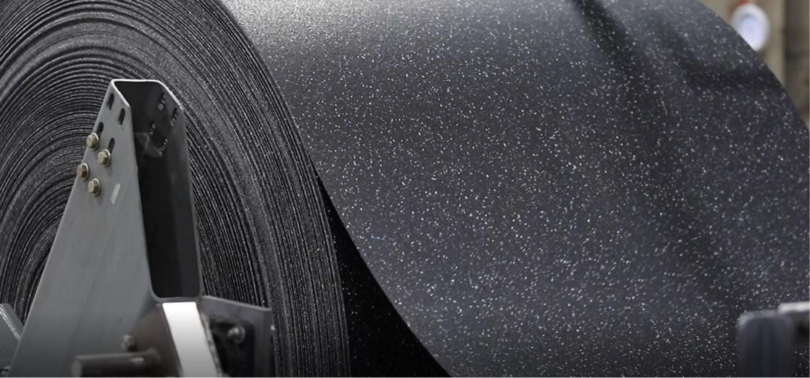 Close-up of a large roll of black rubber material used for industrial purposes, showing texture and speckled design.