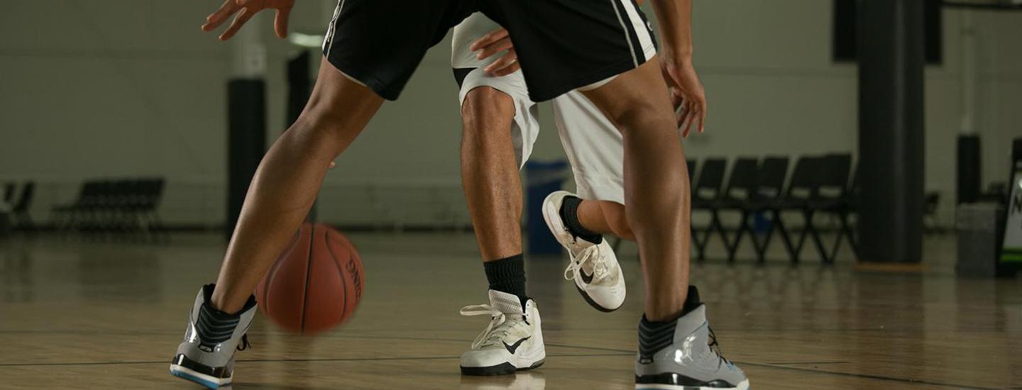 Close-up of basketball players dribbling and defending in an indoor sports court.