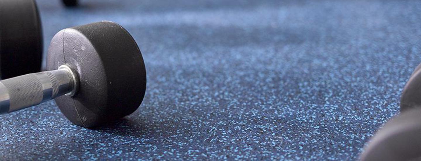 Dumbbell on a speckled blue gym floor, highlighting durable flooring.