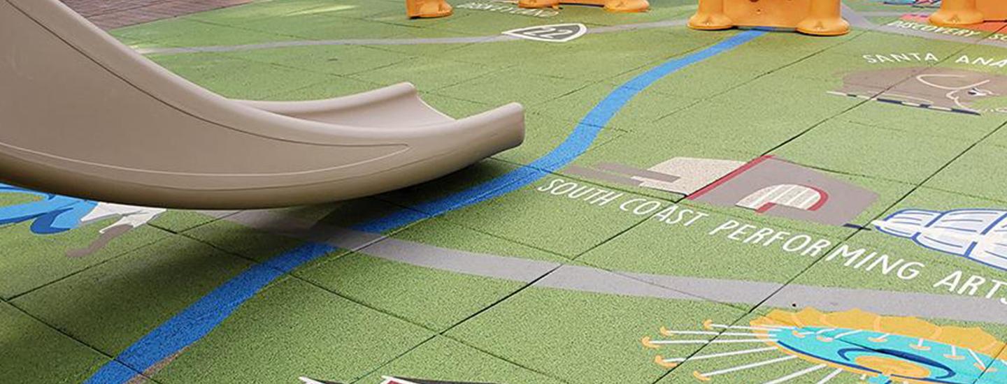 Colorful playground rubber flooring with illustrations and a gray slide.
