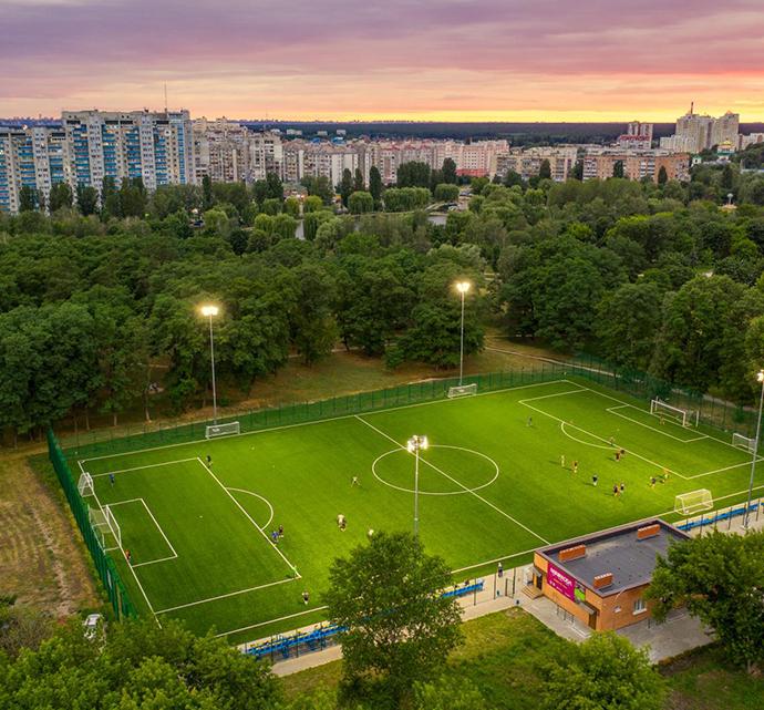 Aerial view of an outdoor soccer field at dusk surrounded by trees and buildings.