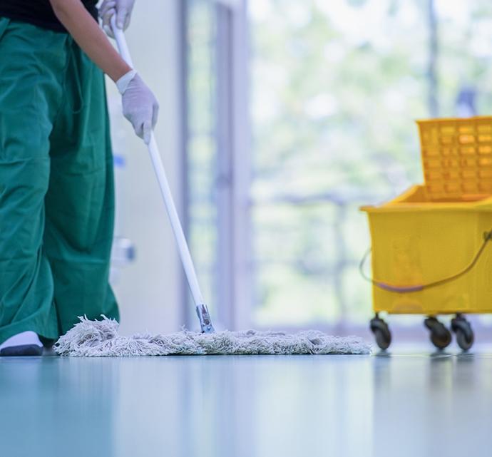 Janitor mopping a shiny floor in a bright room, with a yellow cleaning cart nearby.