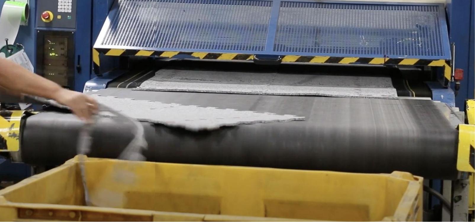 Worker handling a large sheet of rubber material through a machine in an industrial setting.