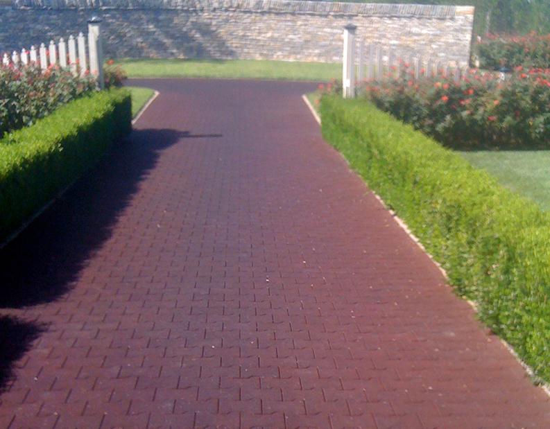 Paved walkway lined with hedges and a white fence leading to a gate.