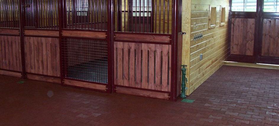 Interior view of a stable with wooden horse stalls and red floor tiles from the PaveSafe Collection.